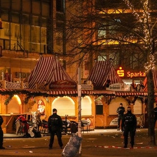 Sicherheitskräfte stehen vor einem abgesperrten Weihnachtsmarkt in Magdeburg.