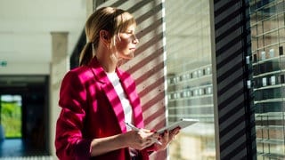 Eine Frau mit Tablet-PC steht an einem Bürofenster.