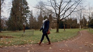 Eine Frau geht im Park. Ihr Gesicht ist unkenntlich gemacht. Sie erzählt, dass ihr Ehemann sie betrogen hat.