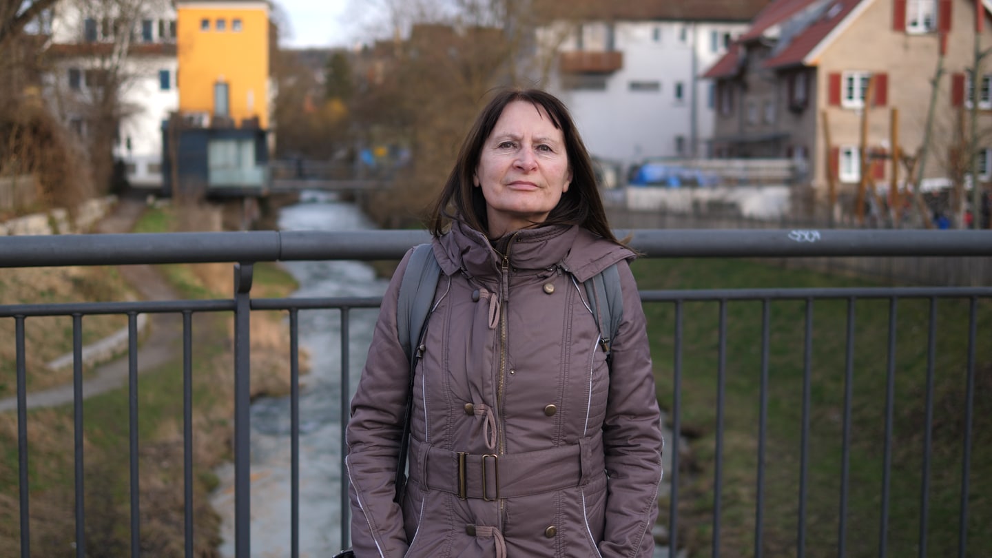 Frau mit braunen Haaren steht auf Brücke, unter der ein kleiner Bach fließt. Herbstliche Anmutung.