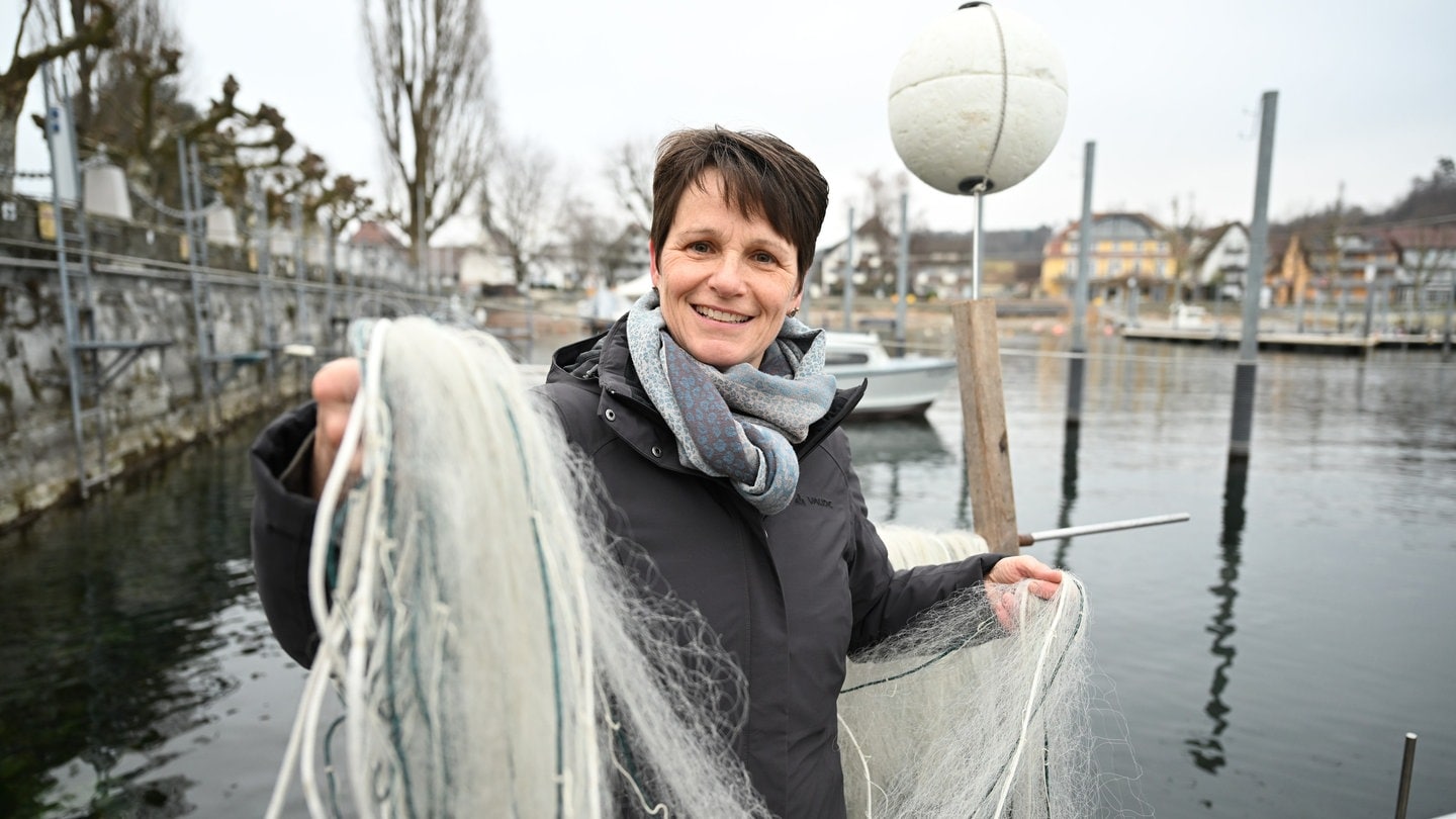 Brünette Frau hält Fischernetz in die Kamera und lächelt.