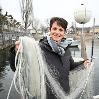 Brünette Frau hält Fischernetz in die Kamera und lächelt.