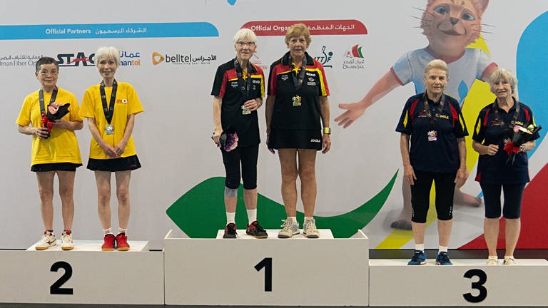 Gruppenbild des Siegertreppchen der Tischtennis-WM der Senioren im Doppel: Heidi steht mit Spielpartnerin auf dem ersten Podest, sie trägt eine goldene Medaille und hält einen Blumenstrauß.