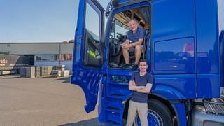 SWR Reporter Julian Camargo und LKW-Fahrer Andreas Selleng sitzen und stehen vor einem blauen LKW und lächeln in die Kamera
