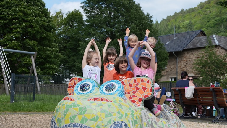 Kinder auf einem großen mit bunten Kacheln beklebten Drachen.
