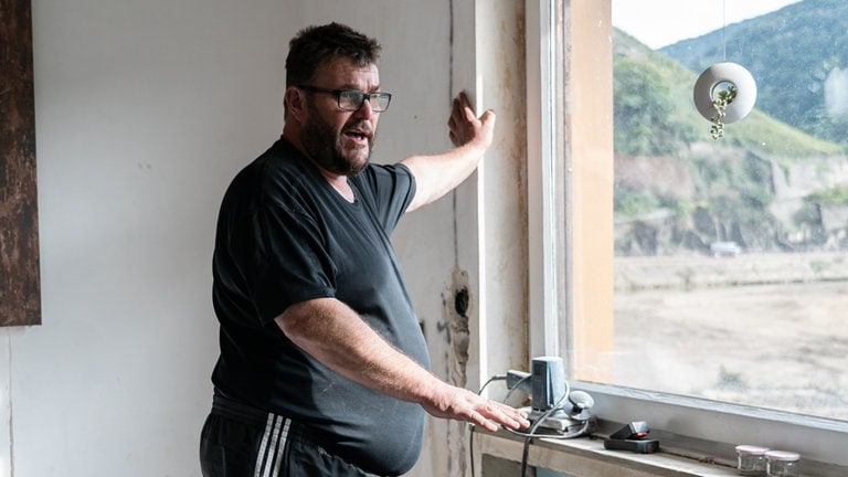 Mann in Zimmer zeigt, mit der Hand, Höhe der Wasserlinie bei der Flut.