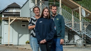 Familie aus Mutter, Vater und Tochter vor ihrem Wohncontainer