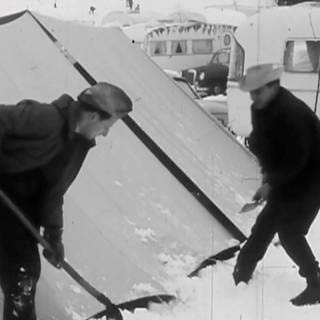 Zwei männlich gelesene Menschen schippen Schnee von einem Zelt