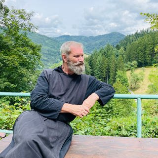 Mann im wallenden Kleid mit grauem Bart sitzt auf Schwarzwaldanhöhe
