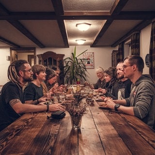 Menschen sitzen im Wohnzimmer an altem Tisch und essen