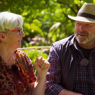 Ein alter Mann und eine alte Frau sitzen auf einer Bank im Garten und unterhalten sich