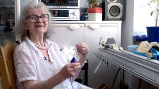 Für ihren Laden hat Gisela 42 Jahre lang gestrickt, gehäkelt und genäht. Sie sitzt in ihrem Wohnzimmer und strickt immer noch weiter. Sie lacht in die Kamera.