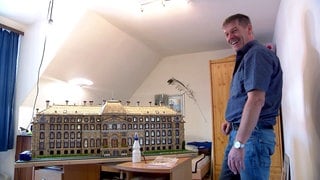 Manfred steht lächelnd neben seiner Modellarbeit aus Streichhölzern: das Schloss Donaueschingen.