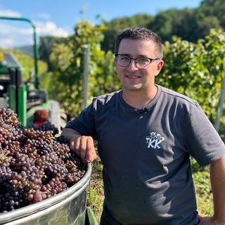 Christopher ist Jungwinzer im Nebenerwerb. Er steht neben einem Tank, der mit Graburgunder gefüllt ist. Er lacht in die Kamera.