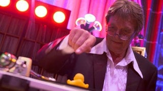 Werner ist 77 Jahre alt und immer noch als DJ aktiv. Er steht hinter dem DJ-Pult und legt Schallplatten auf. Auf einer Schallplatte hat er eine gelbe Quietsche-Ente platziert. 