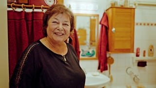 Eine Frau steht in ihrem Badezimmer und lächelt in die Kamera.