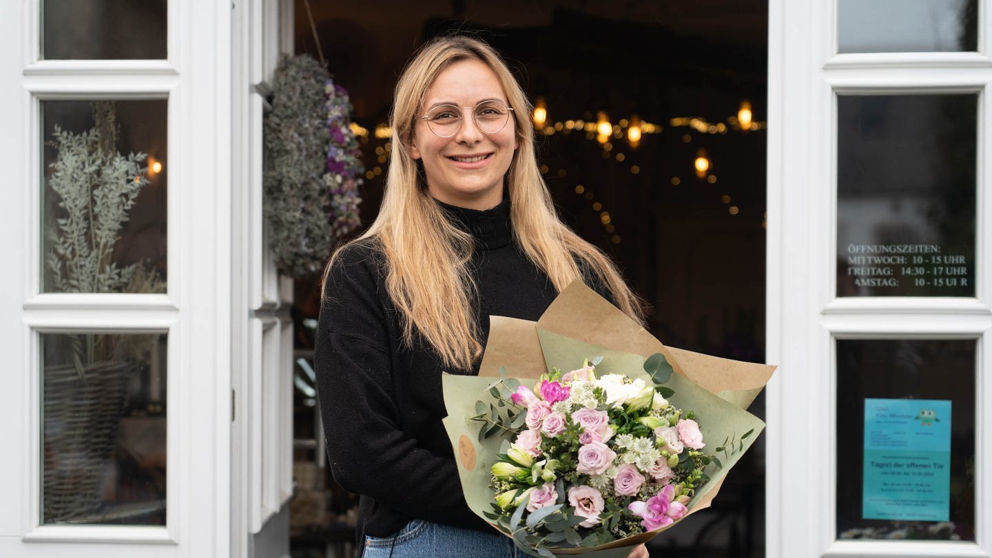 Junge Frau mit Blumenstrauß vor Blumenladen.