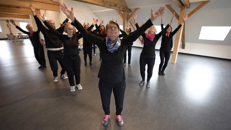 Eine Gruppe Menschen in schwarzen, hautengen Anzügen übt eine Choreographie.