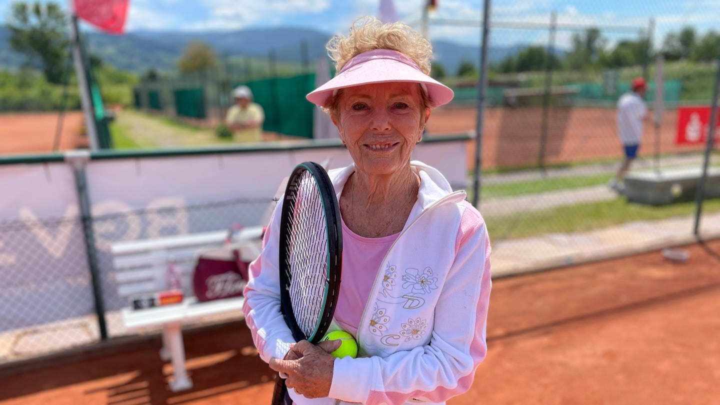 Seniorin steht auf dem Tennisplatz mit Schläger in der Hand