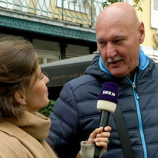 Werner spricht bei der Straßenumfrage in der Karlsruher Innenstadt mit Tici über seine Gefühle und wann er zuletzt geweint hat. Werner hat eine Glatze, ist groß und schaut zu Tici, die ein Mikro in der Hand hält. 