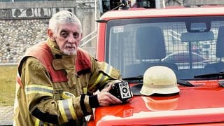 Bertold ist Feuerwehr-Fotograf. Er trägt Feuerwehrbekleidung und hat seine Kamera in der Hand. Er steht neben einem Einsatzwagen und schaut in die Kamera.
