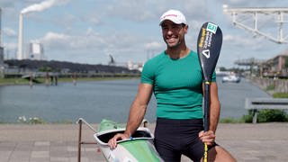 Saeid fährt Kanu und tritt für das Refugee Olympic Team bei den Olympischen Spielen 2024 in Paris an. Er lächelt in die Kamera und hält das Ruder in der Hand.