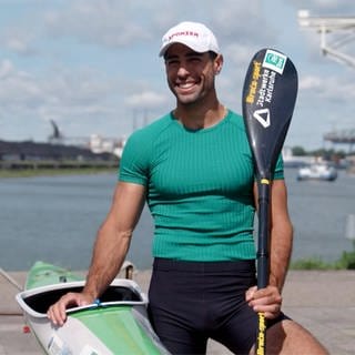 Saeid fährt Kanu und tritt für das Refugee Olympic Team bei den Olympischen Spielen 2024 in Paris an. Er lächelt in die Kamera und hält das Ruder in der Hand.