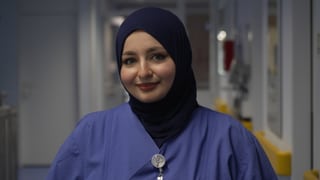 Eine Krankenpflegerin mit Kopftuch steht im Krankenhausflur und lächelt