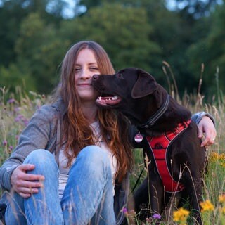 Nicole Kunkel, Frau mittleren Altes, sitzt auf Blumenwiese mit Hündin Lotta