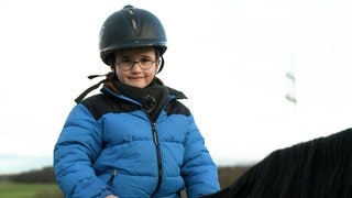 Junge mit Brille in blauer Jacke mit Reiterhelm