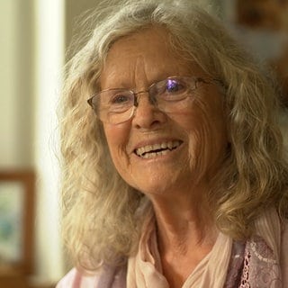 Frau mit langen grauen Haaren und Brille lacht.