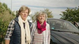 Zwei Frauen, mittleren und älteren Alters, stehen in herbstlicher Kleidung vor einem Auto