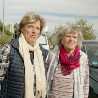 Zwei Frauen, mittleren und älteren Alters, stehen in herbstlicher Kleidung vor einem Auto