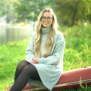 Junge Frau am Flussufer auf dem Rumpf eines Ruderbootes sitzend
