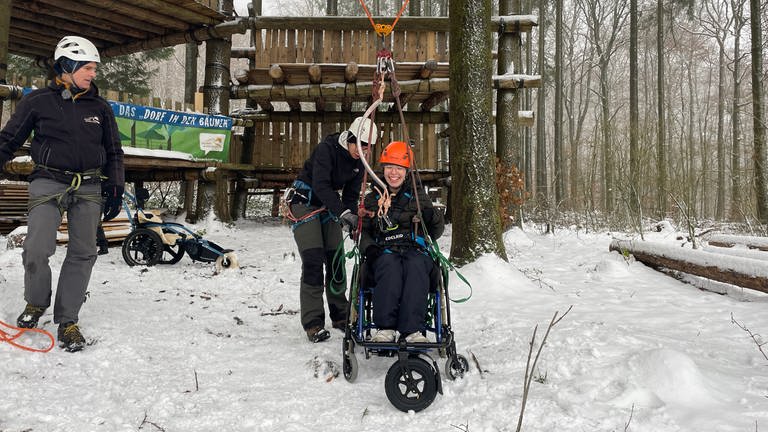 Junge Frau mit Rollstuhl ist mit Seilen an der Baumschaukel befestigt.