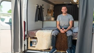 Junger Mann sitzt auf seinem Bett im Camper Van