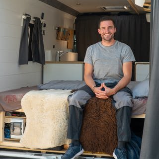 Junger Mann sitzt auf seinem Bett im Camper Van