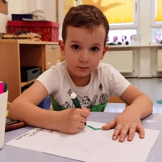 Julian malt im Kindergarten ein Bild mit einem rot-grünen Stern darauf.