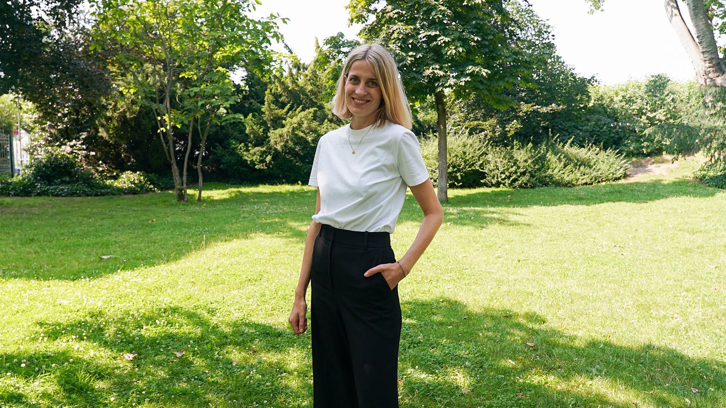 Hannah, Gründerin eines nachhaltigen Modelabels, steht auf einer grünen Wiese.