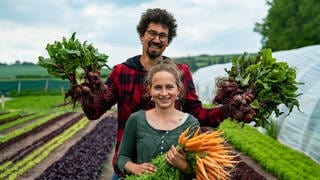 Ein junges heterosexuelles Paar in einem Gemüsegarten mit Gemüse in den Händen