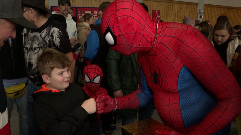 Ein Mann im Spiderman-Kostüm gibt einem Jungen einen Faustcheck zu Begrüßung.