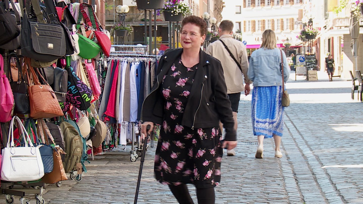 Eine Frau mittleren Alters läuft mit einem Gehstock durch die Fußgängerzone