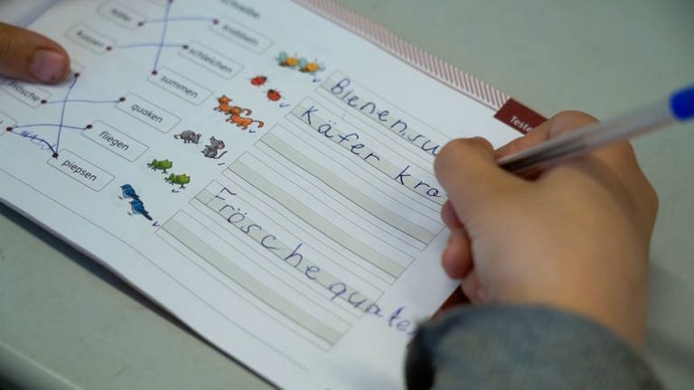 Eine Kinderhand schreibt in ein Schreiblehrbuch.