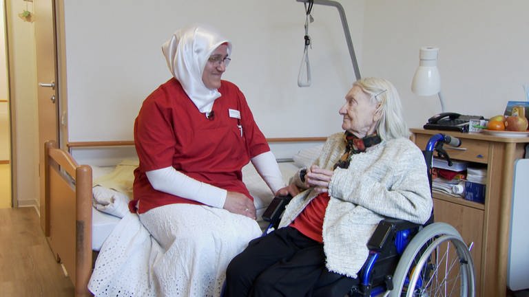 Altenpflegerin sitzt zusammen mit Seniorin in Zimmer in Altenheim.