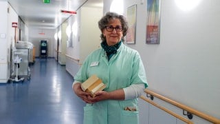 Eine Frau steht in einem Kittel im Flur eines Krankenhauses. Sie ist Grüne Dame im Evangelischen Krankehaus Bad Dürkheim.