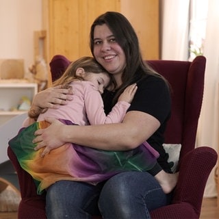 Frau mit braunen Haaren mit Kind auf dem Schoß.