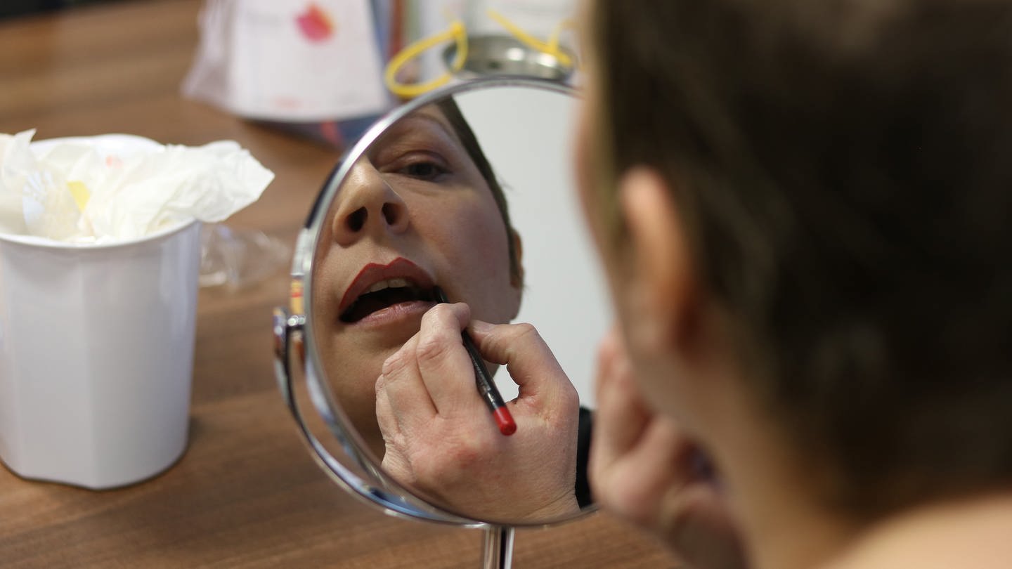 Eine Frau schminkt sich vor dem Spiegel die Lippen.