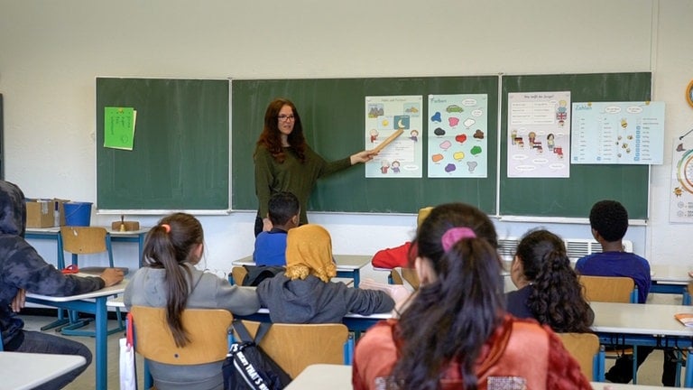 Mitteljunge Lehrerin erklärt etwas an der Tafel vor der Klasse.