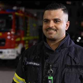 Ein Mann mit Feuerwehranzug steht in einer Feuerwehrwache und lächelt.