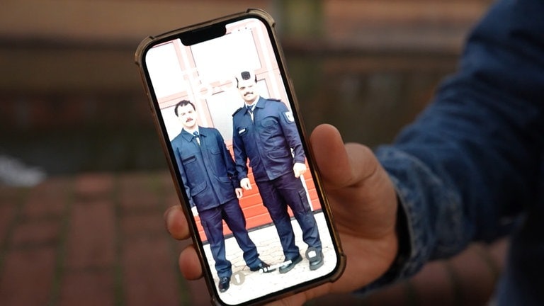 Ein Handy wird in die Kamera gehalten, auf dem Sperrbildschirm sieht man zwei Feuerwehrmänner.